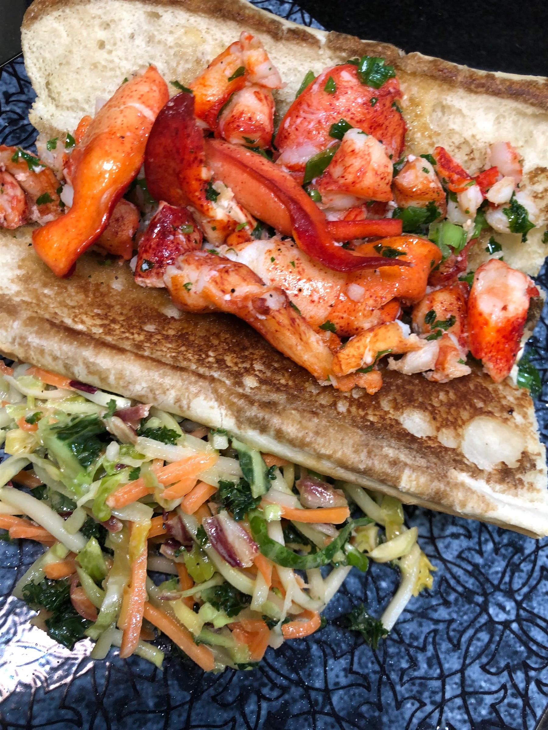 Connecticut Lobster Roll: Delicate lobster meat tossed in warm butter, lemon juice, scallions and parsley served on a toasted lobster roll with a side of super slaw