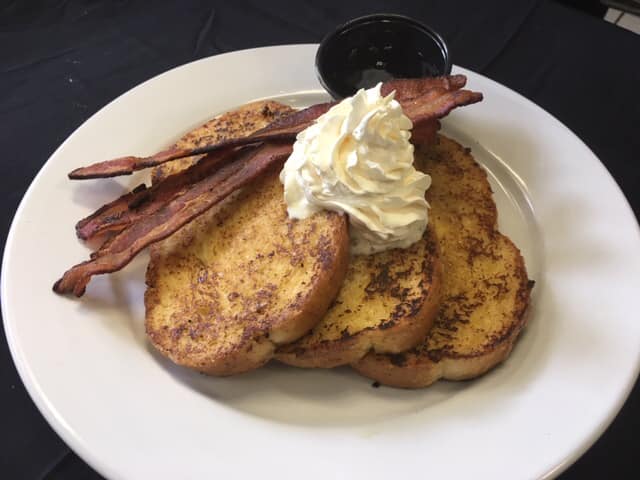 three pieces of french toast with bacon, whipped cream and maple syrup.